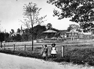 Band stand on Chase Green
Near site of Cenotaph. Photographed from Harrison's Lane, which ran between Chase Side and Chase Hill before the advent of the railway. Now closed and part of Chase Green, where a double line of lime trees marks the position. In the background are the Wesleyan church, built in 1889 and the magistrate's court, built in 1900. St. Paul's Church had not yet been built at the corner of Old Park Avenue and the drive can be seen to Chase Park House, which was demolished when the railway was built. The new bandstand on Chase Green was built in August 1900. The new court house was opened the same year. 
Keywords: bandstands;Chase Green;Trinity Church;magistrates court