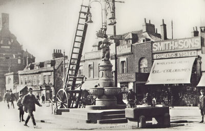 Fountain and fire escape ladder
The fire escape was secured by a chain and padlock. The key was kept at the police station in London Road. "It was found convenient to keep the fire-escape there until the advent of the trams [1909] created the opportunity for the local lads to get a laugh by pushing the apparatus against the overhead wires ..." - [i]History of Enfield[/i] vol.2, p.39
Keywords: fountains;The Town;water troughs;retail