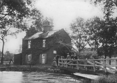 Ha'penny Bridge, about 1914
Inscribed on rear: "Fisherman's Cottage nr. Chingford Old Church. Mrs [and] Mr Mullins last occupier. Now demolished by M.W.B. [Metropolitan Water Board]. Public footpath from Edmonton to Chingford over the bridge. The writer is standing on the bridge with a mac under his arm. Wm. Austin"

Donated by Marjorie Pratt, 1995. Draft reply to her, apparently by David Pam, reads "... It shows the ha'penny bridge which lay on the footpath from Picketts Lock at Edmonton to Chingford Old Church, then in ruins but since restored. The bridge was a favourite resort when I was a chile, especially on B M Ms [Bank Holiday Mondays]. Boys swam in the river there and a number were drowned. It was, as the name implies, once a toll bridge, and the cottage housed the toll collector. The EPS is most pleased to add the photo to its collection." 
Keywords: 1910s;bridges;footpaths;Chingford