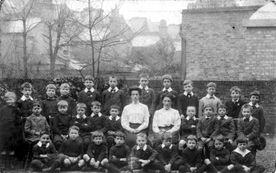 Preparatory School for Boys, 47 Silver Street.
At the corner of Churchbury Lane, the building, previously the Church School of Industry, was Miss Bagshaw's Preparatory School for Boys from 1911 to 1935. 
From an old sepia print on a postcard, one copy posted by F.M.Bagshawe, the taller of the two teachers, on 4th April 1911. The name "H. L. Biggs" on the back may be the photographer. Donated by Mrs N. Read, 9 Fir Tree Walk.
Keywords: schools;people