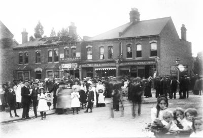 Fire, Chase Side, 18th July 1911
A crowd of people in the street in front of some shops. Some unknown event seems to have attracted them. The left-hand shop is derelict and half of its roof is missing. Shop signs include "W. J. WILLIS / Established 1875", "SPRATTS PATENT", "Drapery THE BEE HIVE. Stores", "126 DECORATORS & UPHOLSTERERS 126", "LAING".

[i] Comment by P Cracknell, 2014-04-01:[/i] The house shown on the left is 'Rosetta' (122 Chase Side) which is now converted to shops (Hanging around, Decorative supplies and The Glass House). This and the adjacent shop (now Highlights hair salon) were subsequently repaired. The righthand shop (126 Chase Side) was later demolished to accommodate the forecourt of the Jet petrol station. The 'Bee Hive' shop is now a residential property. This photo was taken from the western end of Halifax Road. 

[i]Comment by Daren Gordelier, 2014-05-05:[/i] The fire took place on 18th July 1911 and started at 122 Chase Side, it spread to 122a occupied Mr Willis (a corn chandler) at the rear there were two brick / timber store sheds 180ft long which were destroyed. The other properties affected in the photo were 124 Mrs Bullock (linen draper) and 126 Mr Lang a decorator, the contents of both being damaged by water, as was 23 Holtwhites Avenue owned by Mr A Gibson. Fire brigades from Enfield, Ponders End, Southgate, Tottenham and Edmonton attended. Such was the scale of the fire that it drew visitors and the newspaper ran out of copies. 
Keywords: people;roads and streets;shops