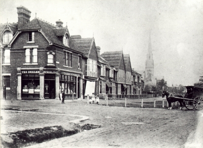 Corner of Chase Side and Chase Green Avenue about 1890
Shop in foreground has signs: "TEA DEALER / STRIBLING / CHEESE-MONGER". The open drain in left foreground appears to lead to culvert under the road.
Note on reverse of print: "Mr J. S. Stribling's father was minister of Zion Chapel 1832-1871 and he died Easter 1882. Mr J. S. Stribling was born in the 1840s. Christ Church (joining of Zion Chapel and Chase Side Chapels) was opened in 1875." The spire of Jesus Church is visible in the distance. There appears to be an open drain or gutter in the left foreground. 

[i]Reproduction right held by Enfield Local Studies Library and Archive.[/i]
Keywords: 1890s;horse-drawn vehicles;shops