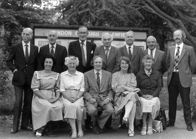 Council of Management 1984/85
Pictured on the seat installed in memory of Reg. Williams (a former Vice President). 
Sitting, left to right: Irene Smith (Hon. Secretary), Priscilla Lowen (Hon. Treasurer), Christopher Jephcott (Architecture & Planning Group), Hilary Stone, Verma Byford (Social events).
Standing: Stan Lowen (Records), Gordon MacFarlane, Donald Potter (President), Alan Skilton (Chairman), Derek Needham, Wally Woodfield (Trees Group), Stuart Mills (Footpaths & Open Spaces Group).
Missing from the picture are Valerie Carter (Vice President and Newsletter Editor), Denis Hoy, Len Keeble (Historic Buildings Group), Pam Mills, David Pam and Derrick Stone.
Keywords: 1980s;people;seats;LP1;Enfield Preservation Society;EPS;committee