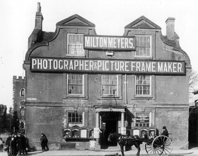 Former Greyhound Inn, Enfield Town
Signs indicate use by Milton Meyers, Photographer & Picture Frame Maker, but posters wrapped round the pillars outside the door appear to read "... Business ... removed..." Lettering on the righ-hand ground floor window reads "The Enfield Independent Building Society office". The building was demolished in 1897 and later replaced by a bank.
Keywords: 1890s;demolished buildings;horse-drawn vehicles;horses;pubs