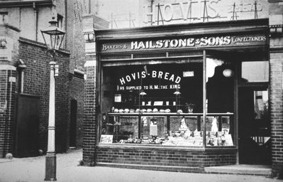 Hailstone & Sons, bakers and confectioners, Southbury Road
Nearly opposite Stanley Road. Note on back of print reads: "Note the early timing mechanism at the top of the gas lamp post. Also cottage and Coburg shape loaves in the shop window, the cottage in two parts and the Coburg in one, both circular in shape. The Coburg had a cut across the top which opened out on baking. The large loaves were 2 lbs in weight and the weight was often made up with an extra piece of bread which we thought tasted better than the main loaf."
Keywords: bakeries;Southbury Road;shops;gas;lamps;street furniture